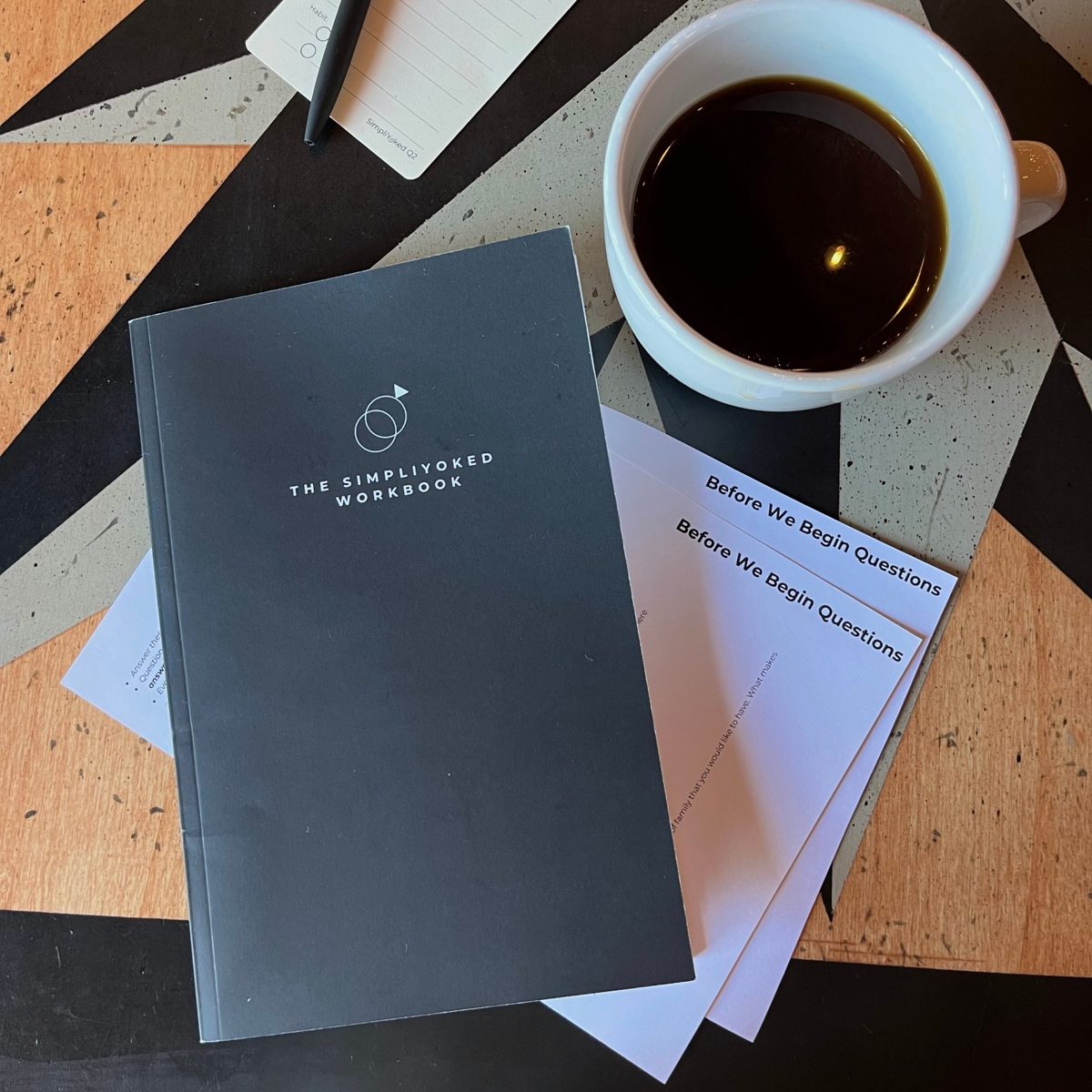 The SimpliYoked workbook and Before We Begin questions on a cafe table with coffee